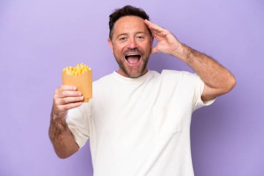 Orta yaşlı beyaz bir adam elinde patates kızartması tutuyordu. Mor fırında izole edilmiş, sürpriz bir ifadeyle.