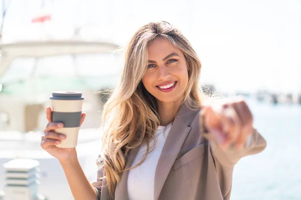Ładna Blondynka Urugwajska Kobieta Trzyma Kawę Świeżym Powietrzu Wskazuje Palcem — Zdjęcie stockowe