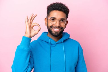 Pembe arka planda gözlüklü ve iyi bir işaret veren Brezilyalı genç adam.
