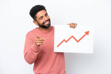 Young Brazilian man isolated on white background holding a sign with a growing statistics arrow symbol and pointing to the front