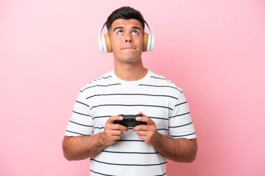 Genç yakışıklı bir adam pembe arka planda izole edilmiş bir bilgisayar oyunu kontrolörüyle oynuyor.