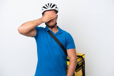 Beyaz arka planda izole edilmiş termal sırt çantalı beyaz tenli genç bir adam gözlerini elleriyle kapatıyor. Bir şey görmek istemiyorum.