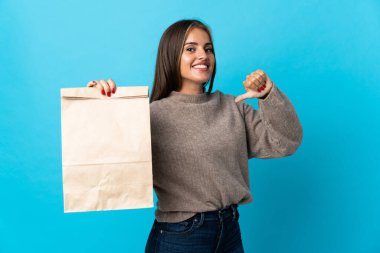 Mavi arka planda bir paket yiyecek alan bir kadın gururlu ve kendini beğenmiş.