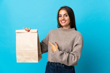 Bir paket yiyecek alan bir kadın mavi arka planda izole edilmiş.