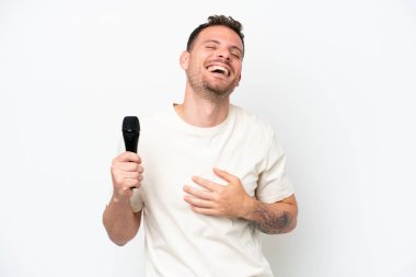 Beyaz arka planda izole edilmiş bir mikrofonu eline alan beyaz tenli şarkıcı çok gülümsüyor.