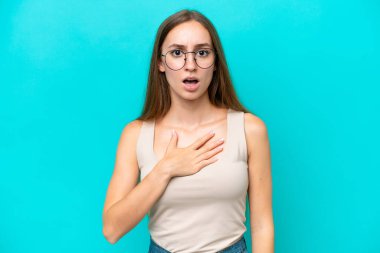 Mavi arka planda izole edilmiş genç beyaz kadın sağa bakarken şaşırdı ve şok oldu.