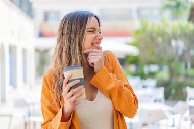 Genç ve güzel bir kadın açık havada kahvesini yudumlarken bir fikir üretiyor ve etrafına bakıyor.