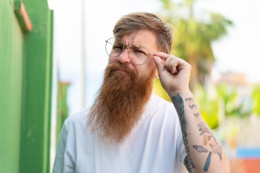 Kızıl saçlı, sakallı, gözlüklü ve hayal kırıklığına uğramış bir adam.