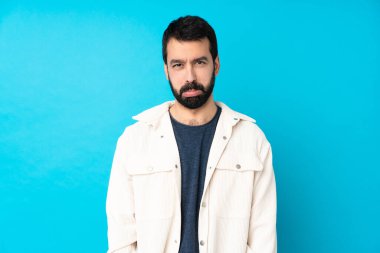 Beyaz kadife ceketli genç ve yakışıklı bir adam. Hüzünlü ve depresif bir ifadeyle izole edilmiş mavi arka plan.