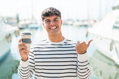 Genç İspanyol bir adam açık havada kahve alıp bir ürün sunmak için kenarı işaret ediyor.