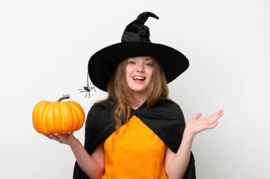 Cadı kılığında genç bir kadın kostümü beyaz arka planda izole edilmiş bir balkabağı tutuyor ve şok olmuş yüz ifadesi var.