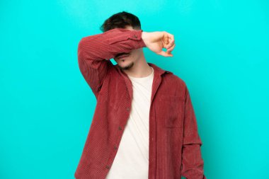 Beyaz tenli yakışıklı adam mavi arka planda izole edilmiş gözleri elleriyle kapatıyor.