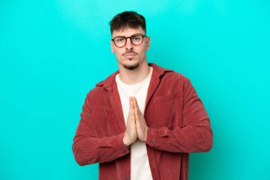 Mavi arka planda izole edilmiş beyaz tenli yakışıklı adam avuç içlerini bir arada tutuyor. İnsan bir şey ister.