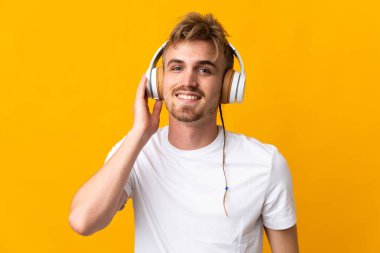 Sarı arka planda izole edilmiş yakışıklı sarışın adam müzik dinliyor.