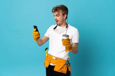 Genç elektrikçi, izole olmuş bir duvarın üzerinde kahve ve bir cep telefonu tutuyor.