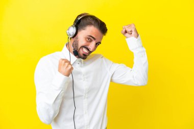 Tele pazarlamacı beyaz adam sarı arka planda izole edilmiş bir kulaklıkla çalışarak zaferi kutluyor.