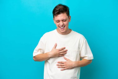 Genç ve yakışıklı Brezilyalı bir adam mavi arka planda izole edilmiş, gülümsüyor.