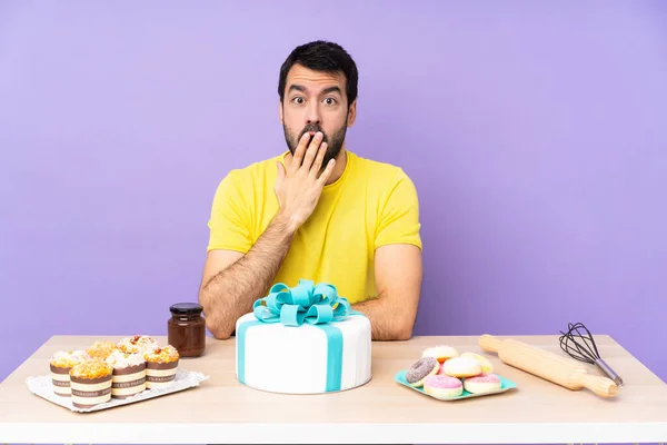 Man in a table with a big cake surprised and shocked while looking right