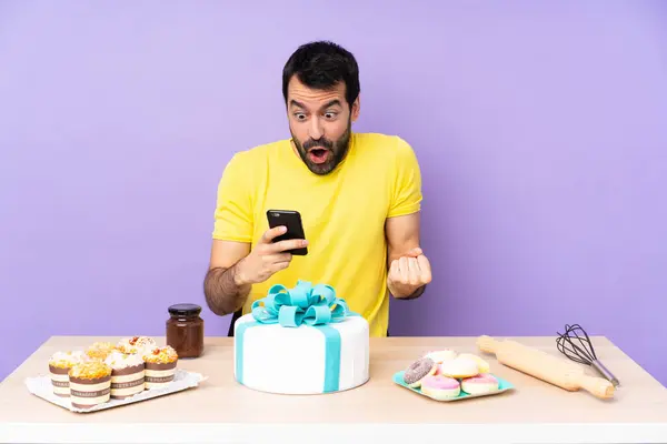Man in a table with a big cake surprised and sending a message
