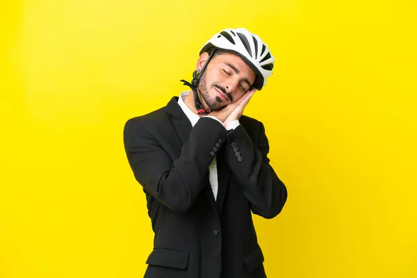Business caucasian man with a bike helmet isolated on yellow background making sleep gesture in dorable expression