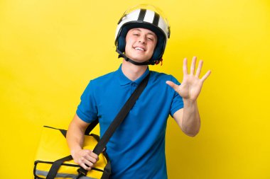 Sırt çantalı genç Brezilyalı adam sarı arka planda izole edilmiş, parmaklarıyla beşi sayıyor.