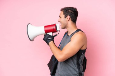 Spor çantalı genç beyaz adam pembe arka planda izole edilmiş megafonla bağırıyor.