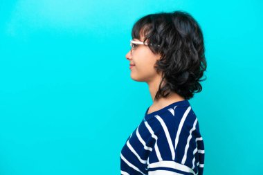 Genç Arjantinli kadın mavi arka planda gözlüklü.