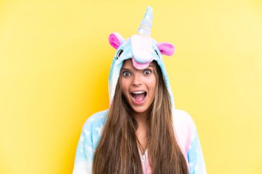 Tek boynuzlu bir pijama giyen beyaz bir kadın sarı arka planda, şaşırmış bir yüz ifadesiyle izole edilmiş.