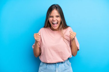 Mavi arka planda izole edilmiş genç beyaz kadın galibiyeti kutluyor.