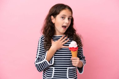 Küçük beyaz kız elinde dondurma tutuyor pembe arka planda izole edilmiş şaşırmış ve şaşırmış bir halde sağa bakarken.