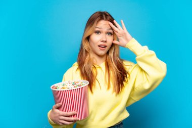 Soyutlanmış mavi arka planda patlamış mısır tutan genç kız.