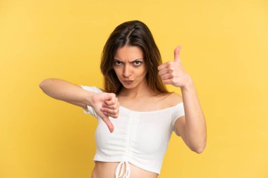 Sarı arka planda izole edilmiş beyaz bir kadın iyiye-kötüye işaret veriyor. Evet ya da hayır arasında kararsız