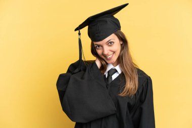 Genç üniversite mezunu, sarı arka planda tek başına gülüyor.