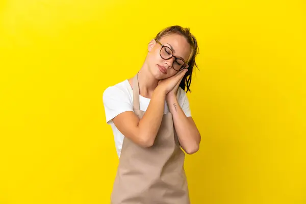 Restaurant waiter Russian girl isolated on yellow background making sleep gesture in dorable expression