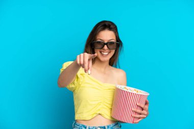 Mavi arka planda 3 boyutlu gözlüklü ve elinde patlamış mısırla gezen beyaz bir kadın.