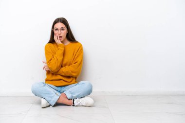 Beyaz arka planda yalnız başına yerde oturan genç kız şaşırmış ve şok olmuştu.