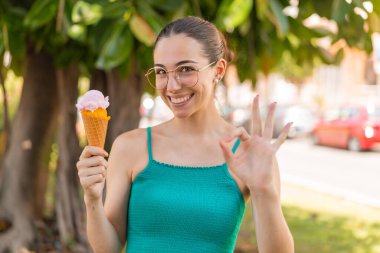Açık havada kornet dondurması olan genç ve güzel bir kadın parmaklarıyla işaret veriyor.