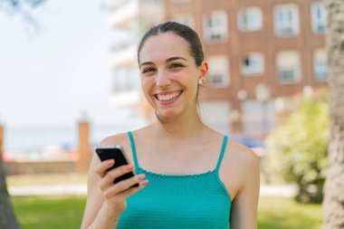 Dışarıda cep telefonu kullanan genç ve güzel bir kadın çok fazla gülümsüyor.