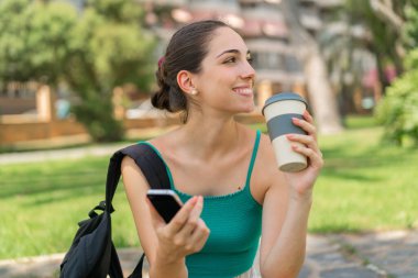 Dışarıda cep telefonu kullanan ve elinde kahve tutan genç ve güzel bir kadın.