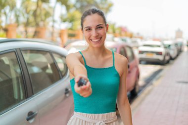 Genç, güzel bir kadın arabanın anahtarlarını tutarken mutlu bir ifadeyle.