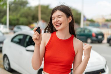 Genç, güzel Ukraynalı kadın açık havada araba anahtarı tutuyor ve zaferi kutluyor.