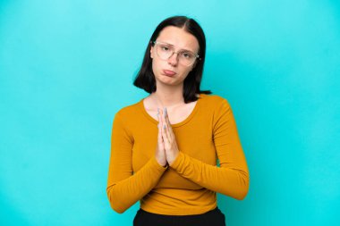 Mavi arka planda izole edilmiş genç beyaz kadın avuç içlerini bir arada tutuyor. İnsan bir şey ister.