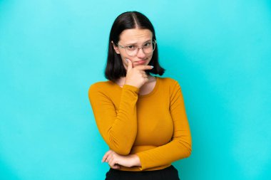 Kafkasyalı genç bir kadın mavi arka planda izole edilmiş. Şüpheleri var.