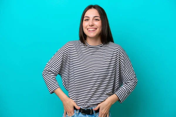 Mavi arka planda izole edilmiş genç beyaz kadın gülüyor.