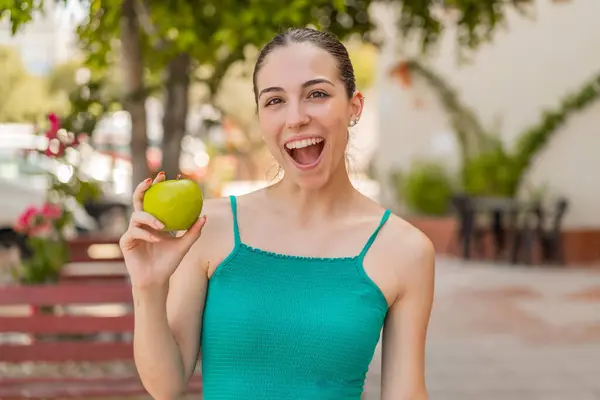 Dışarıda elmalı genç ve güzel bir kadın. Şaşırmış ve şok olmuş bir yüz ifadesi var.