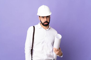 Miğferli genç bir mimar ve hüzünlü bir ifadeyle izole edilmiş mor arkaplan üzerinde planlar tutuyor.