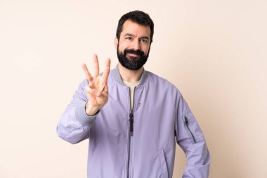 İzole edilmiş arka planda ceket giyen beyaz adam mutlu ve parmaklarıyla üçe kadar sayıyor.