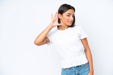 Beyaz arka planda izole edilmiş genç beyaz kadın elini kulağına koyarak bir şeyler dinliyor.