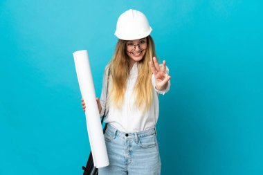 Kasklı ve elinde mavi arka planda izole edilmiş planları olan genç mimar kadın mutlu ve parmaklarıyla üçe kadar sayıyor.