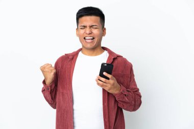 Genç Ekvadorlu adam beyaz arka planda cep telefonu kullanarak ve zafer jesti yaparak izole edildi.